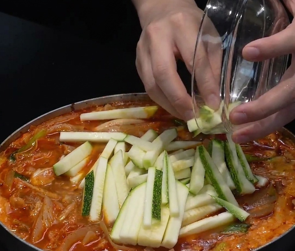 Zucchinischeiben und gehackte grüne Chilis werden oben auf die rote Meeresfrüchtesuppe gegeben.