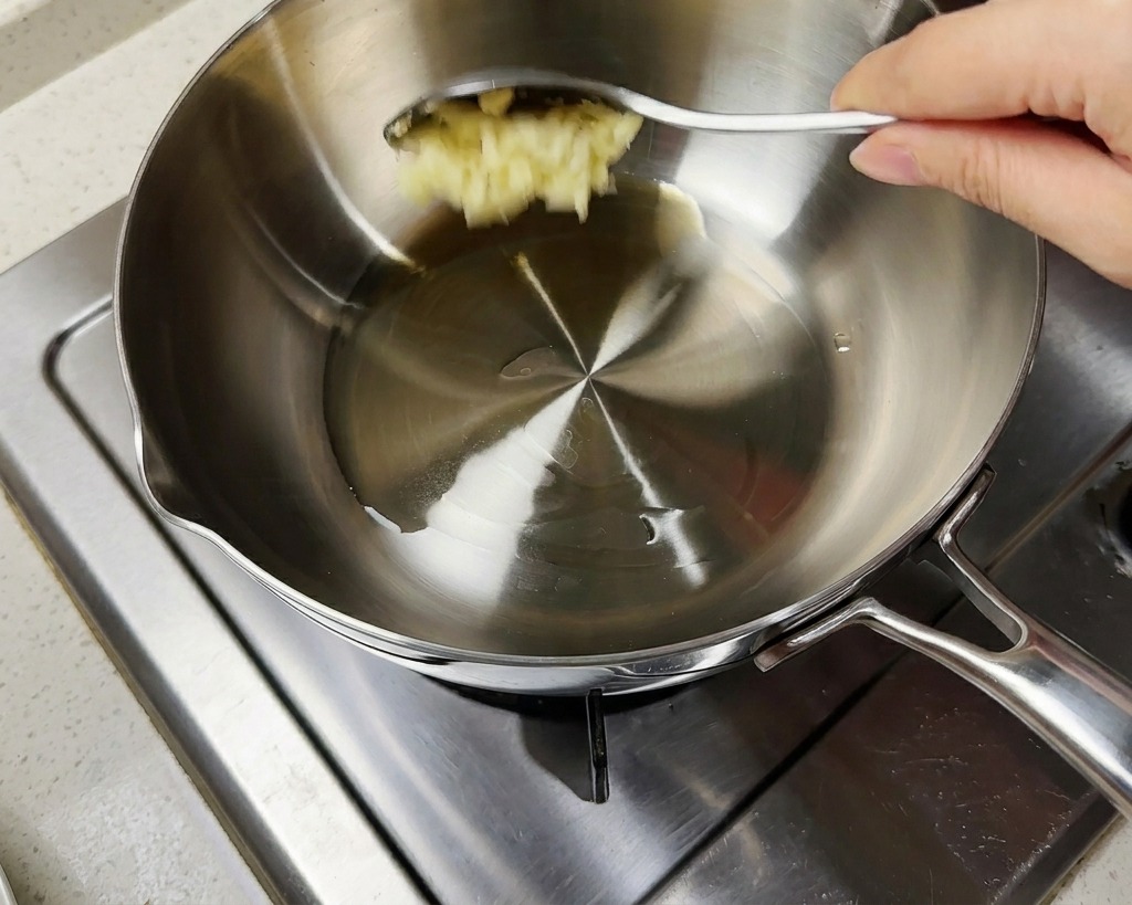 Ein Löffel gehackter Knoblauch wird in einen Topf mit heißem Öl und Frühlingszwiebeln gegeben.