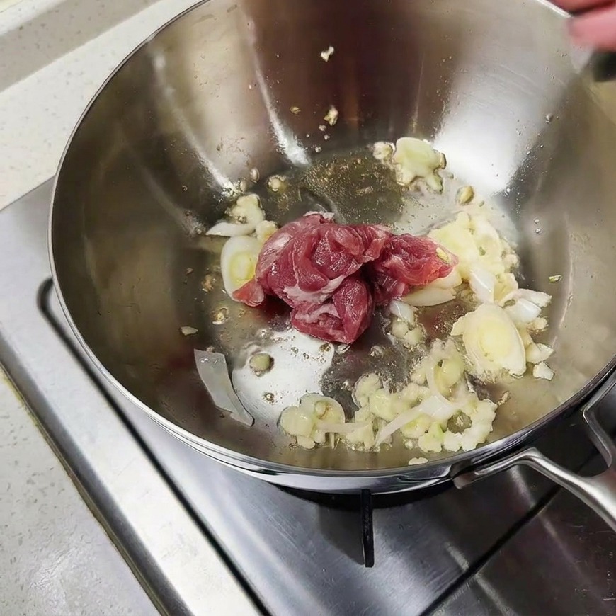Rohe Schweinefleischstücke werden mit Knoblauch und Zwiebeln im Topf angebraten.