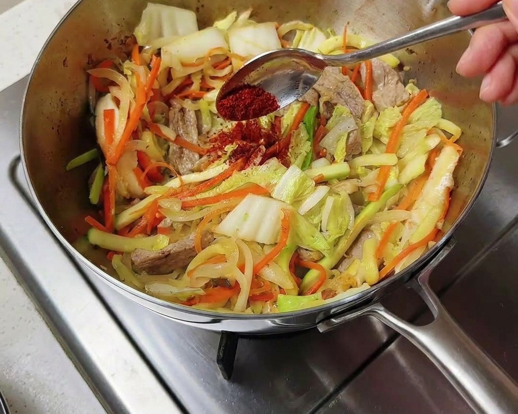 Rotes koreanisches Chilipulver wird über das Gemüse im Topf gestreut.