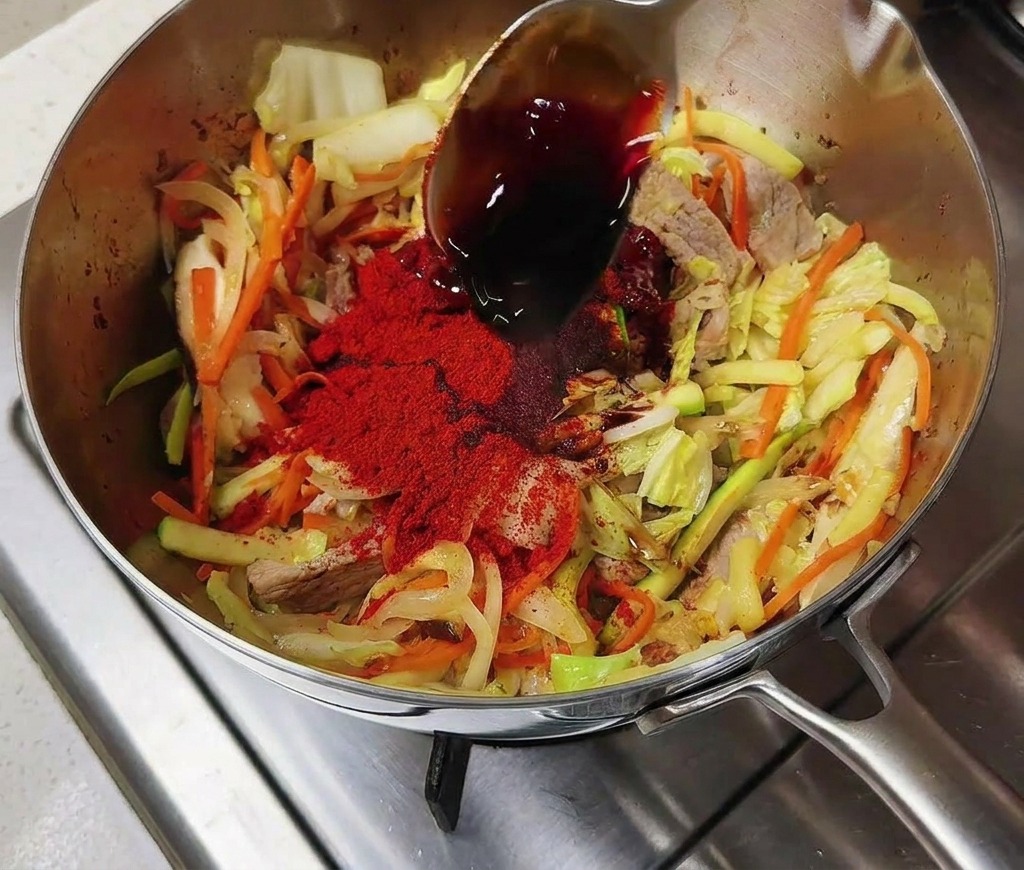 Sojasauce wird über das rote Chilipulver und das Gemüse im Topf gegossen.