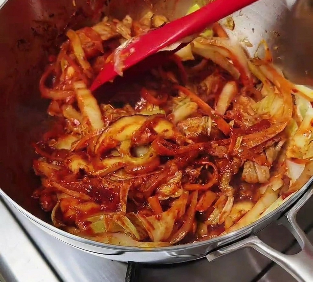 Ein Pfannenwender mischt das Fleisch und Gemüse, das komplett mit roter Würzpaste überzogen ist.