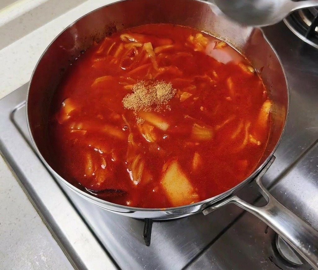 Eine kleine Menge Rinderbrühpulver in der Mitte einer köchelnden roten Brühe.