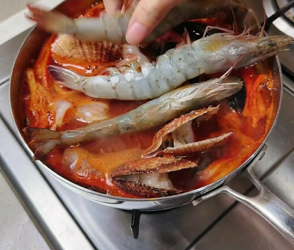 Große rohe Garnelen werden in den Topf mit der kochenden Suppe gelegt.