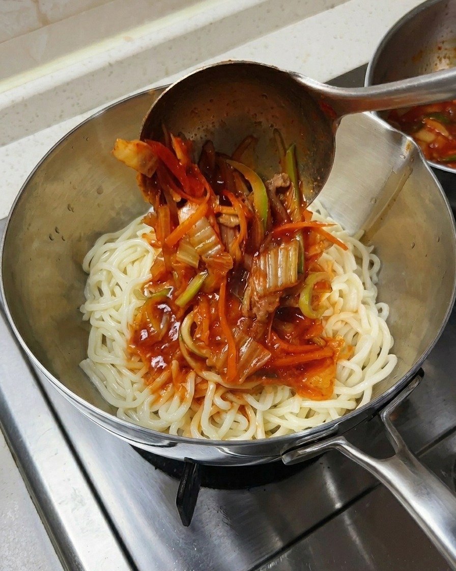 Eine Kelle gießt scharfe Meeresfrüchtesuppe über dicke weiße Nudeln in einer Schüssel.