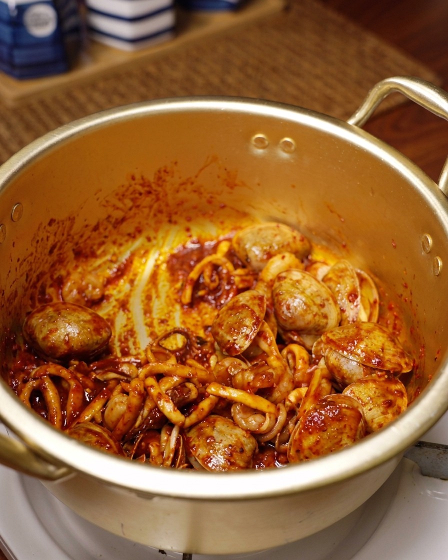 In leuchtend rotem Chili gewendete Meeresfrüchte werden in einem traditionellen goldenen Topf angebraten.
