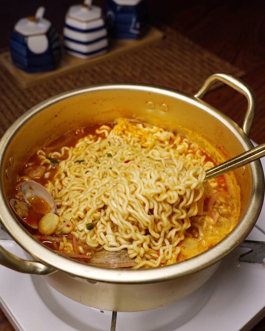 Gewellte Ramen-Nudeln werden mit einem Löffel aus der köchelnden roten Brühe gehoben.