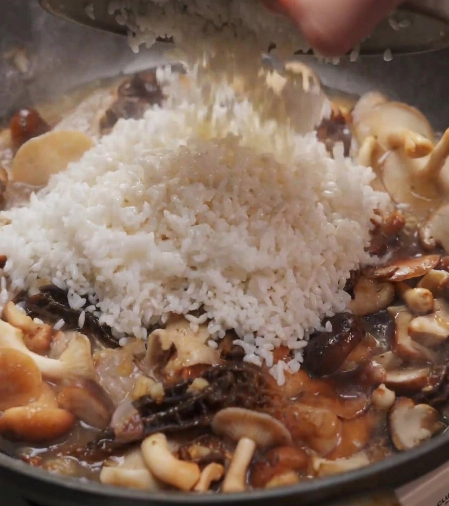 Ein Haufen weißer Reis wird aus einer Schüssel in eine Pfanne mit gedünsteten Shiitake- und Morchelpilzen geschüttet.