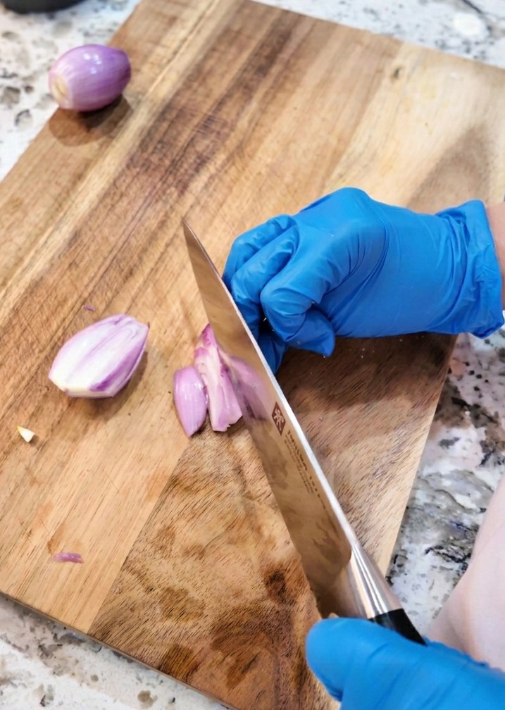 Ein Küchenmesser schneidet lila Schalotten in feine Ringe auf einem Holzbrett.