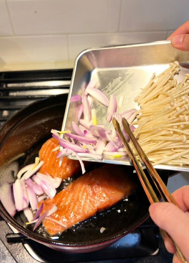 Geschnittene Schalotten werden in einen Topf gegeben, in dem Lachsfilets gerade in Öl anbraten.