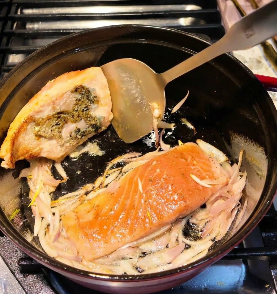 Ein Metallwender wendet ein Lachsfilet im Topf und zeigt eine goldbraun gebratene Oberfläche.