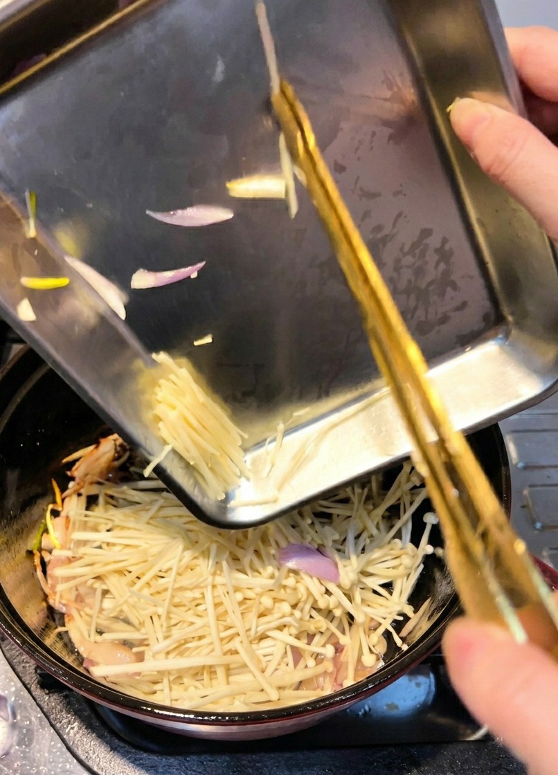 Enoki-Pilze werden in den Topf gegeben, um kurz mit den gedünsteten Schalotten angebraten zu werden.