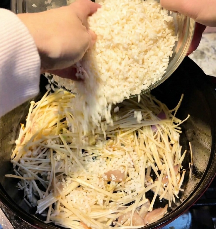 Zwei Tassen weißer Reis werden aus einer Schüssel in den Topf zu den Pilzen geschüttet.