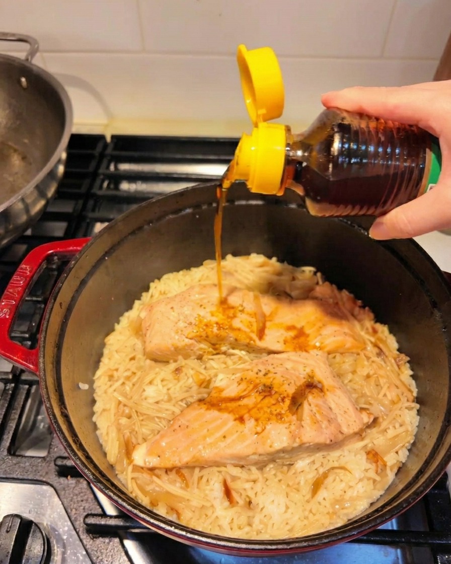 Geröstetes Sesamöl wird über den fertigen Lachs-Reis-Topf geträufelt.