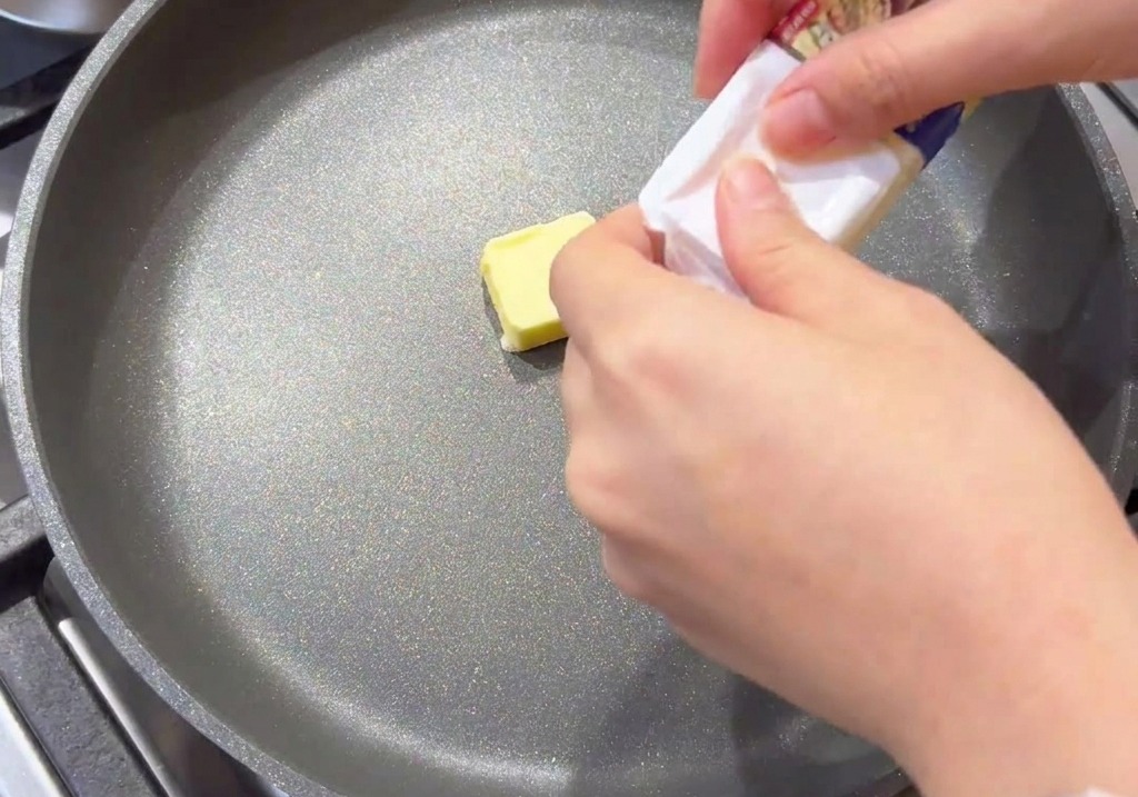 Ein kleines Stück gelbe Butter schmilzt in der Mitte einer grauen, beschichteten Bratpfanne.