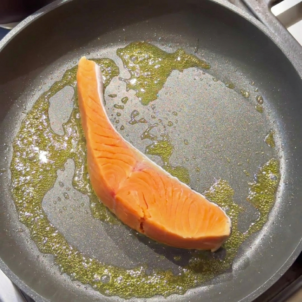 Ein rohes Lachsfilet brät in einer Pfanne mit schäumender, geschmolzener Butter.