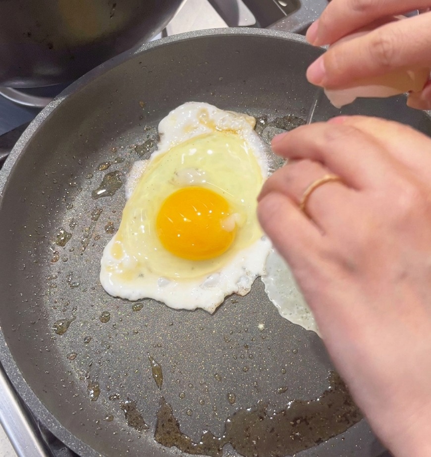 Ein Ei wird in eine beschichtete Pfanne geschlagen, um es zu Rührei zu verarbeiten.