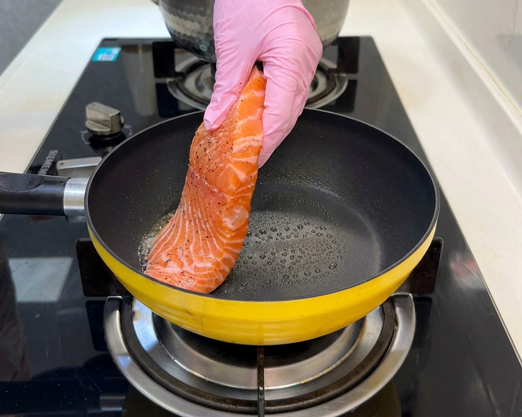 Ein gewürztes Lachsfilet wird in eine erhitzte gelbe Pfanne gelegt.