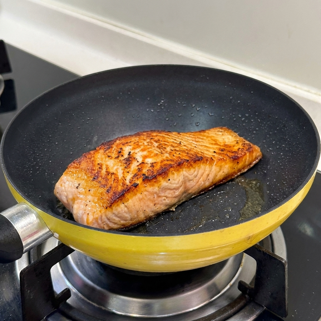 Ein angebratenes Lachsfilet mit perfekt gebräunter, knuspriger Oberfläche in einer gelben Pfanne.