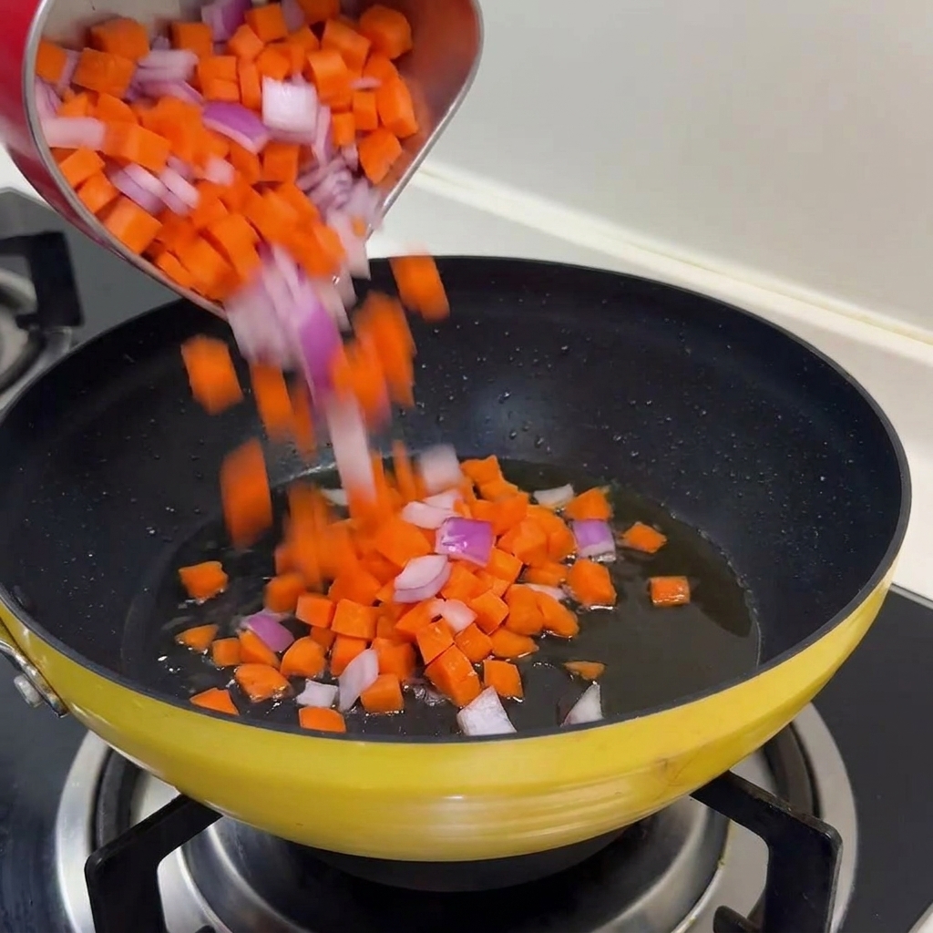 Karotten- und Zwiebelwürfel werden in der Pfanne mit dem restlichen Öl gedünstet.