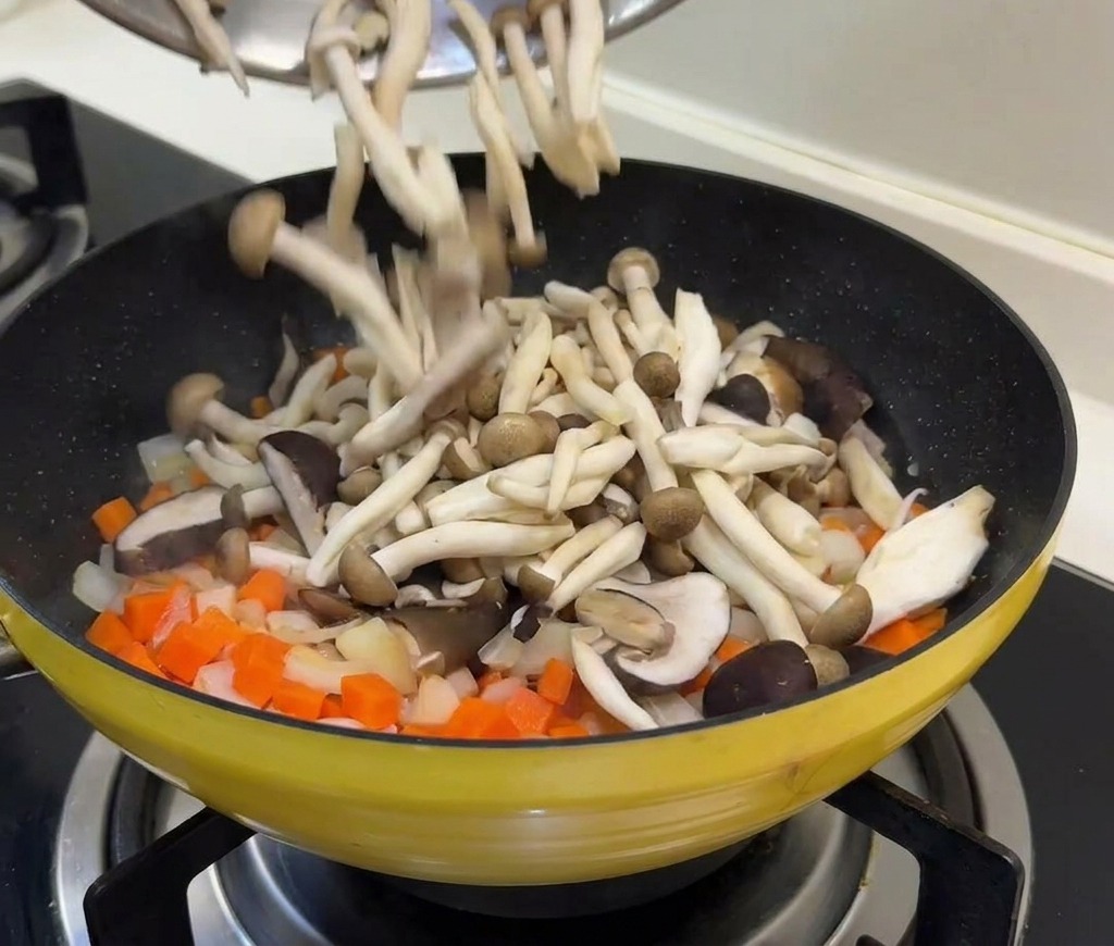 Frische Pilze und Erbsen werden zu den gedünsteten Karotten und Zwiebeln in die Pfanne gegeben.