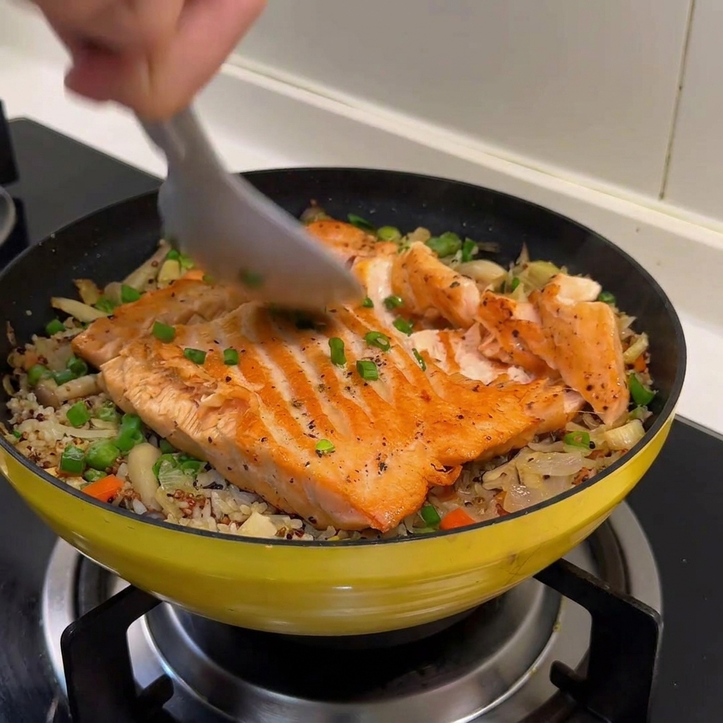 Ein Löffel teilt das gegarte Lachsfilet in grobe Stücke auf dem Reis.