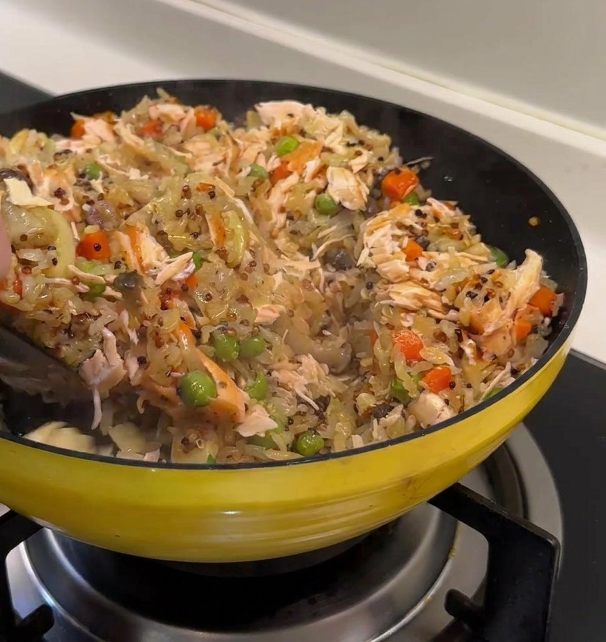 Lachsflocken werden vorsichtig unter den bunten Quinoa-Reis gehoben.