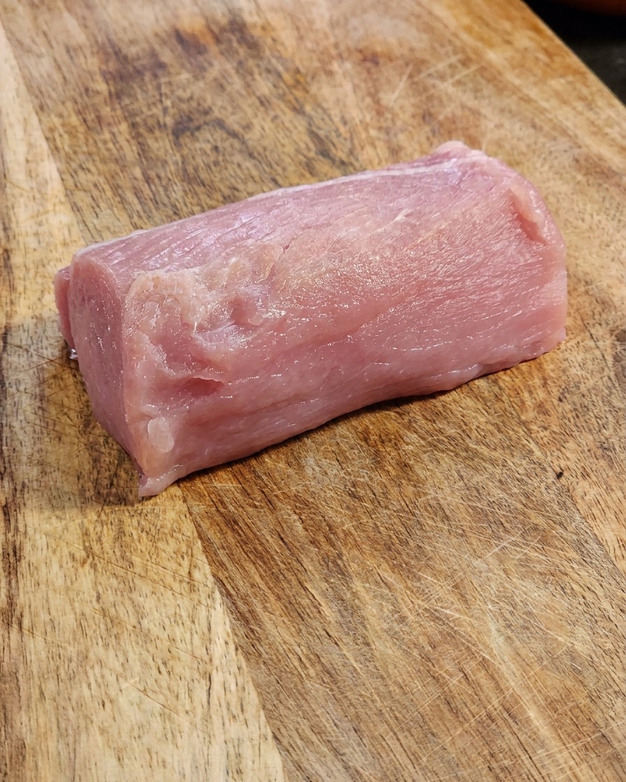 Ein frisches Stück Schweinerücken liegt auf einem Holzschneidebrett.