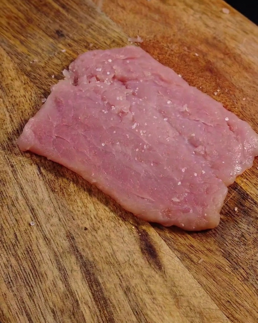 Salz und Pfeffer auf einer flachgeklopften Scheibe Schweinefleisch.