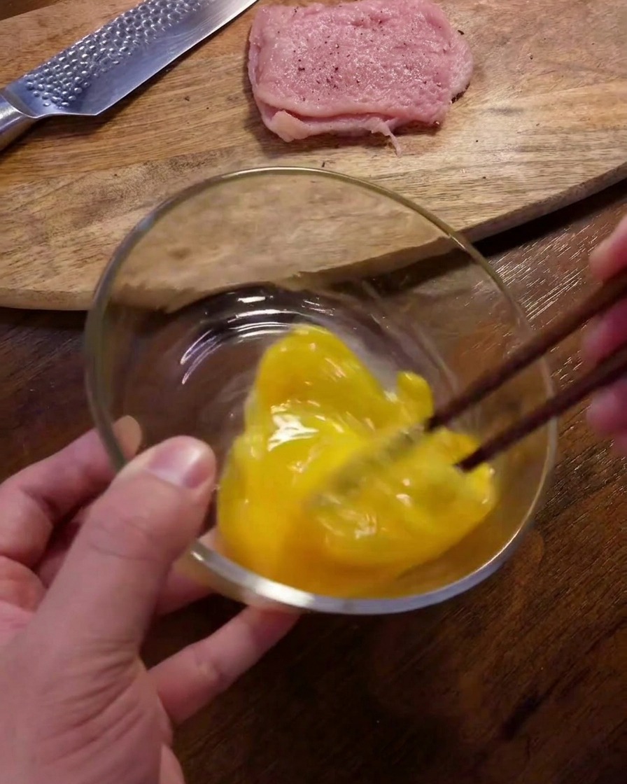 Eier werden mit Stäbchen in einer Glasschüssel auf einem Holztisch verschlagen.