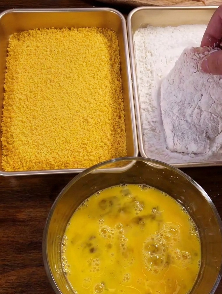Ein Schnitzel wird in einer Schale mit weißer Maisstärke gewendet.