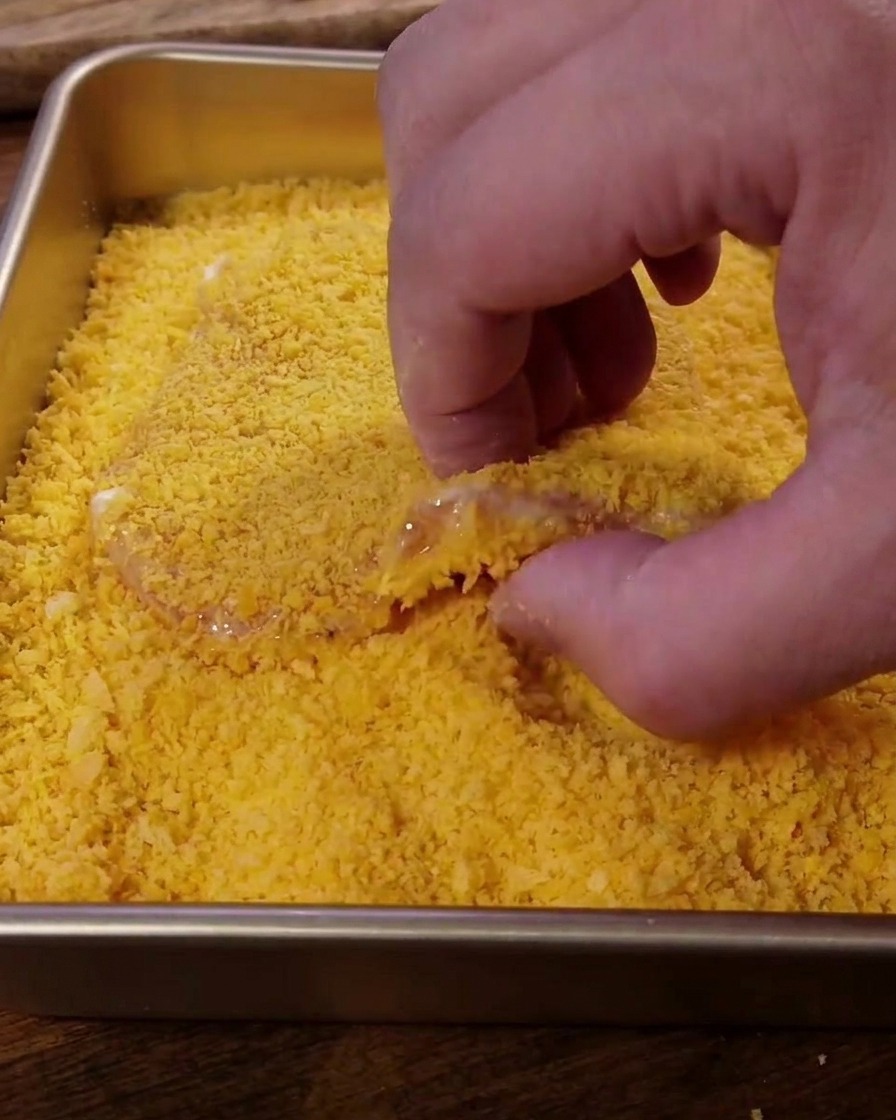 Das Fleisch wird fest in eine Schale mit goldenen Panko-Brotkrümeln gedrückt.
