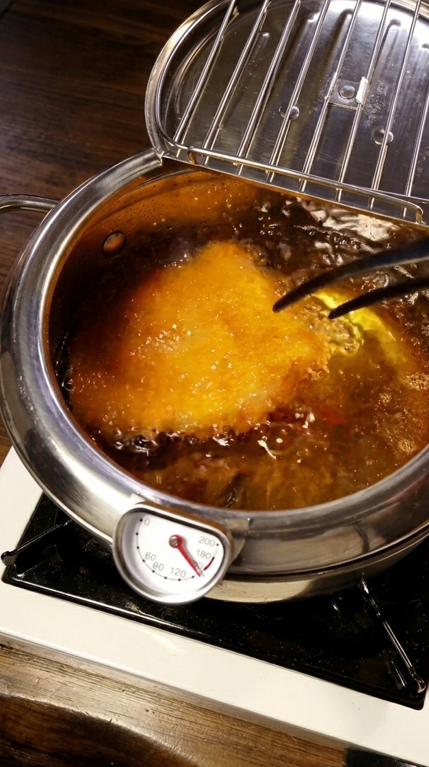 Das Schnitzel frittiert in heißem Öl, ein Thermometer ist sichtbar.