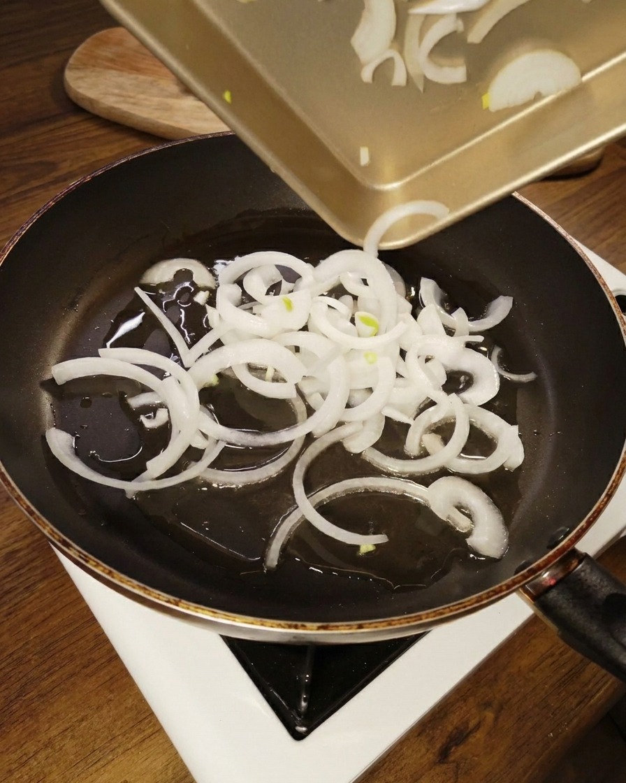 Weiße Zwiebelringe werden in eine Pfanne mit erhitztem Öl gegeben.