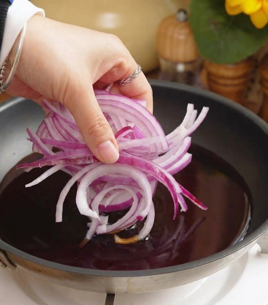 Geschnittene rote Zwiebeln werden in eine Pfanne mit köchelnder dunkler Sauce gegeben.