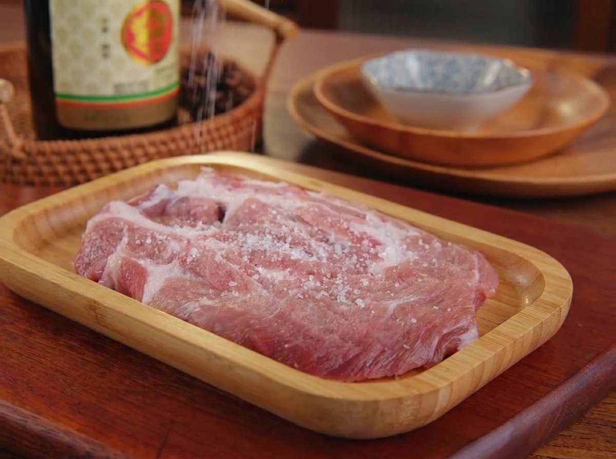 Salz und schwarzer Pfeffer werden auf ein rohes Stück Schweinefleisch gestreut.