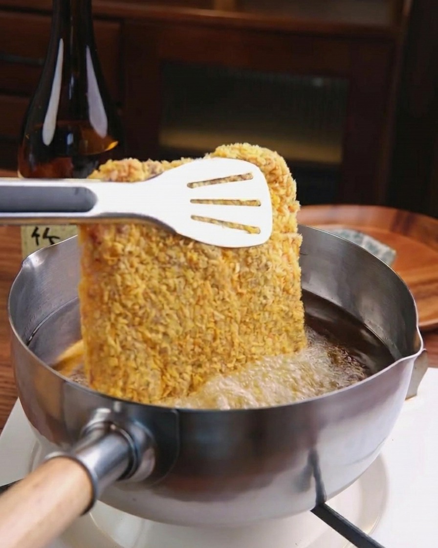 Ein paniertes Schnitzel wird vorsichtig in heißes, sprudelndes Öl in einem Edelstahltopf gleiten gelassen.