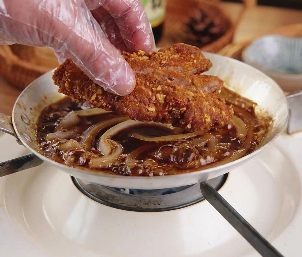 Das geschnittene Schnitzel wird auf die köchelnden Zwiebeln in der Pfanne gelegt.