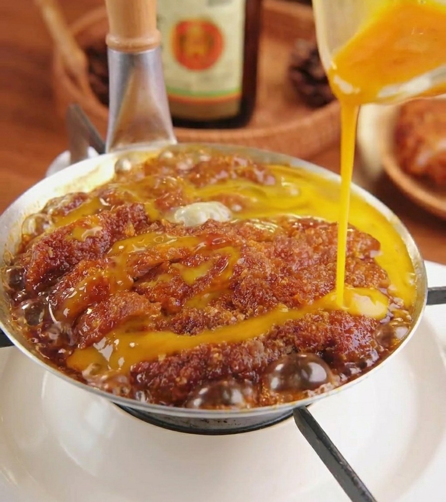 Verquirltes Ei wird kreisförmig über das Fleisch in der Pfanne gegossen.