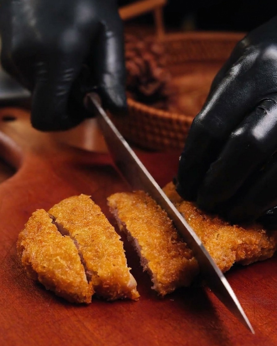 Ein scharfes Messer schneidet ein knuspriges, goldbraunes Schnitzel auf einem Holzbrett in Streifen.