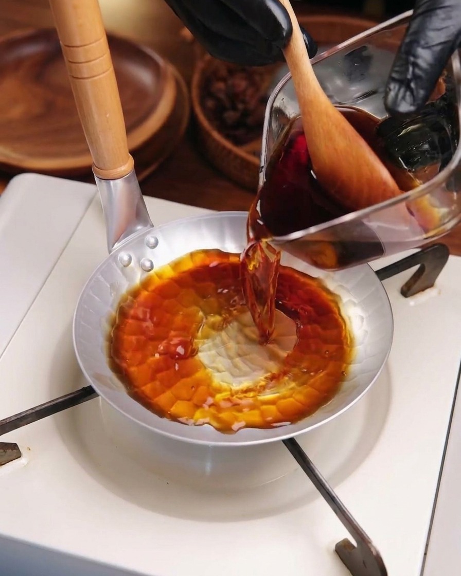 Dunkle Katsudon-Sauce wird in eine kleine Metallpfanne auf einem Kocher gegossen.