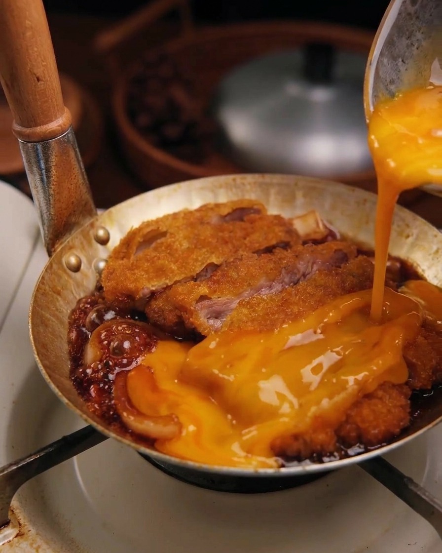 Verquirltes Ei wird über das Schnitzel in der Pfanne gegossen.