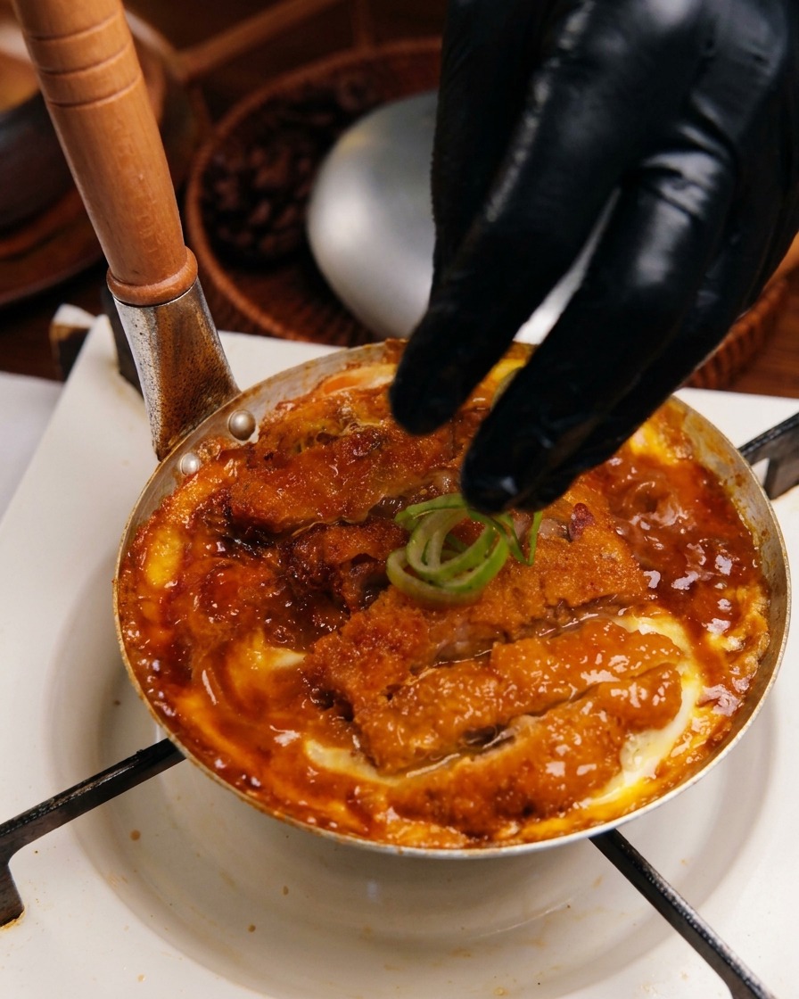 Frische Frühlingszwiebelringe werden über das fertige Katsudon in der Pfanne gestreut.