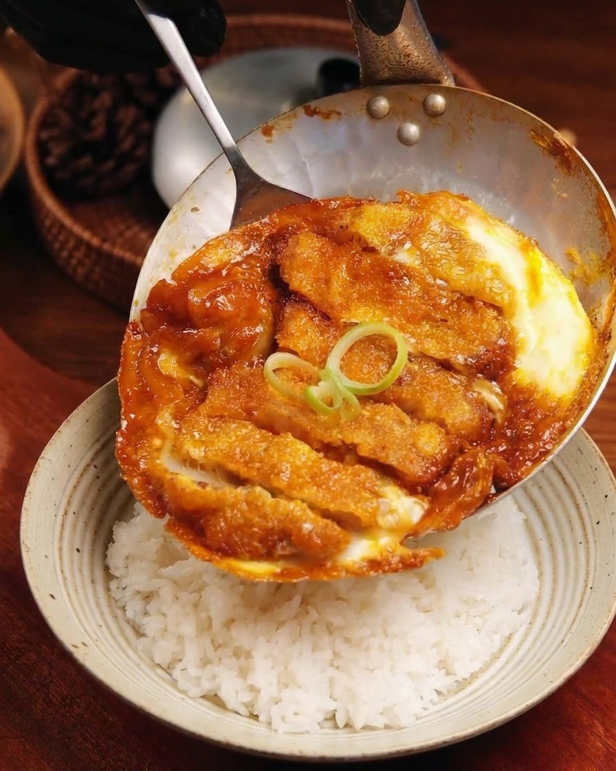 Die fertige Schnitzel-Ei-Mischung wird vorsichtig aus der Pfanne auf eine Schüssel mit Reis geschoben.