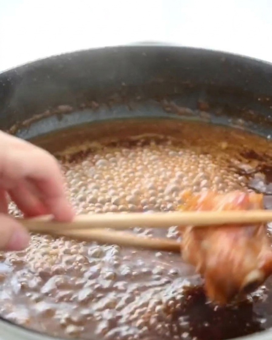 Hähnchenschenkel köcheln in einer blubbernden, dunkelbraunen Honigsauce, während Dampf aufsteigt.
