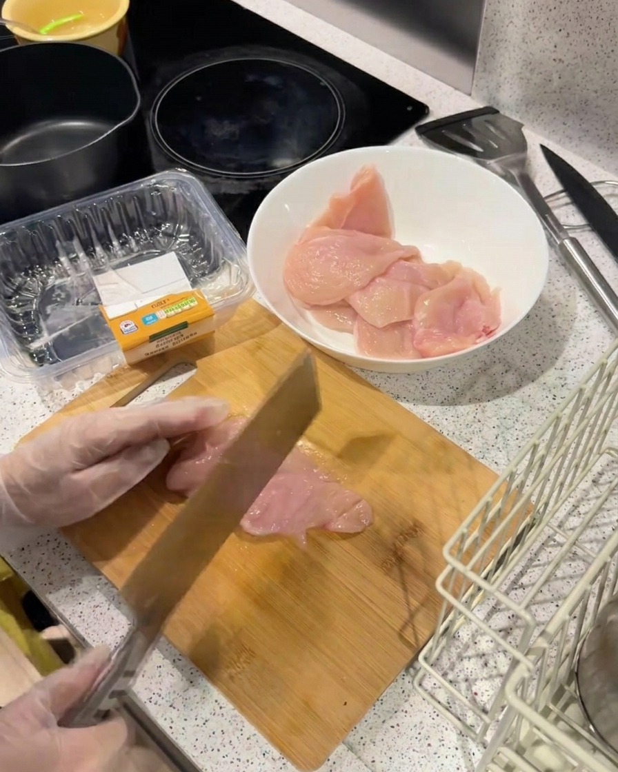 Die Rückseite eines schweren Messers wird verwendet, um ein dünnes Hähnchenfilet auf einem Holzbrett zu klopfen und zu zarten.