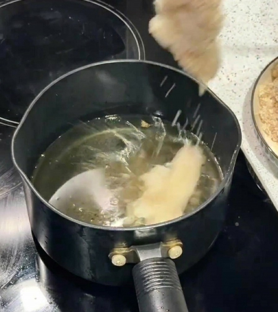 Ein paniertes Hähnchenfilet wird mit Stäbchen vorsichtig in einen Topf mit sprudelndem heißem Öl gelegt.