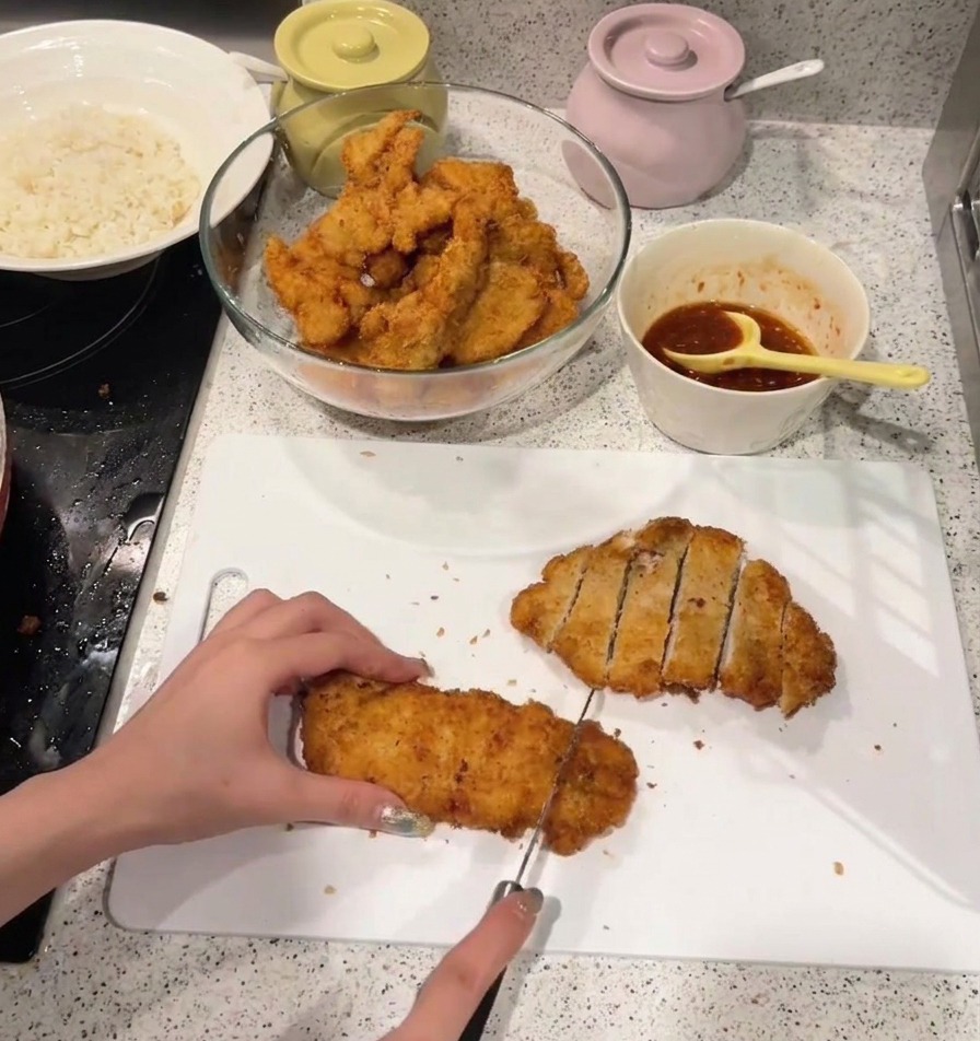 Ein knuspriges, goldbraun frittiertes Hähnchenschnitzel wird auf einem weißen Schneidebrett in Streifen geschnitten.
