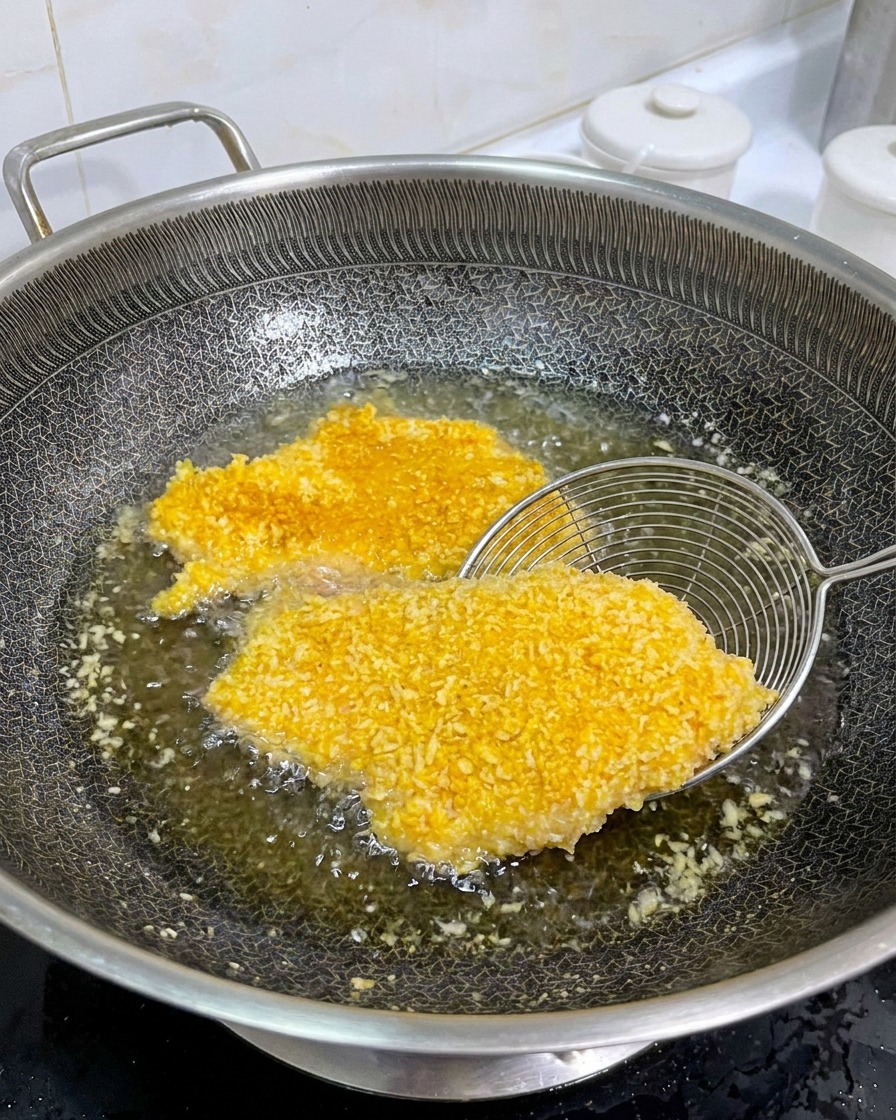 Ein Metallsieb zeigt die perfekt gebräunte Seite des Hähnchenschnitzels in der Pfanne.