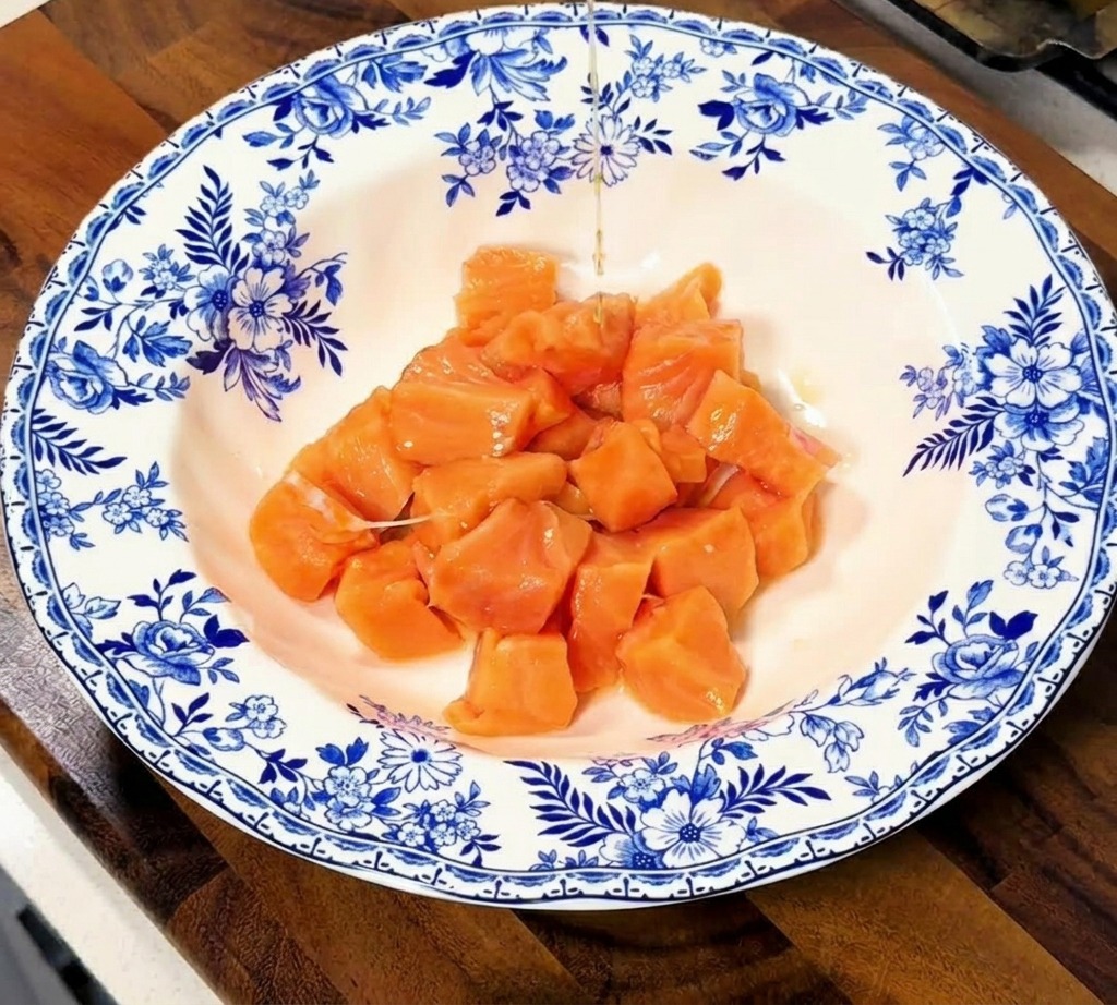 Sojasauce und Sake werden über die Lachswürfel in einer dekorativen Keramikschüssel gegossen.